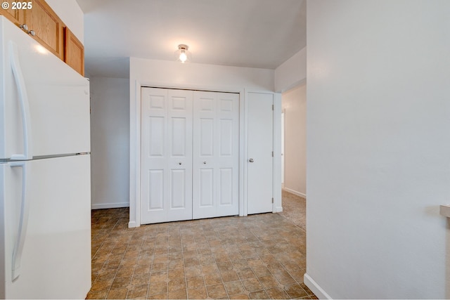 interior space with a closet, freestanding refrigerator, stone finish floor, and baseboards