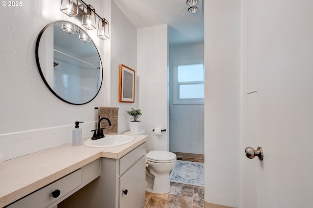 full bathroom featuring toilet, stone finish flooring, and vanity