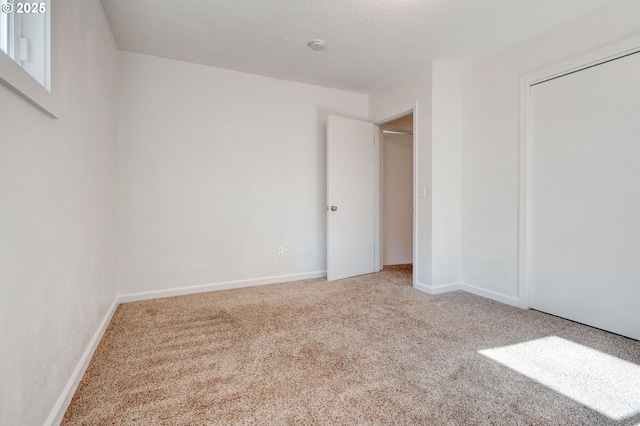 unfurnished bedroom featuring a textured ceiling, carpet floors, a closet, and baseboards