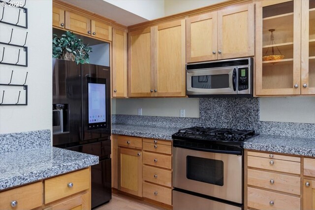 kitchen with glass insert cabinets, light stone countertops, appliances with stainless steel finishes, and backsplash