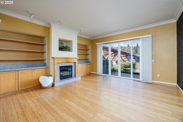 unfurnished living room featuring built in shelves, a premium fireplace, light wood-type flooring, and crown molding