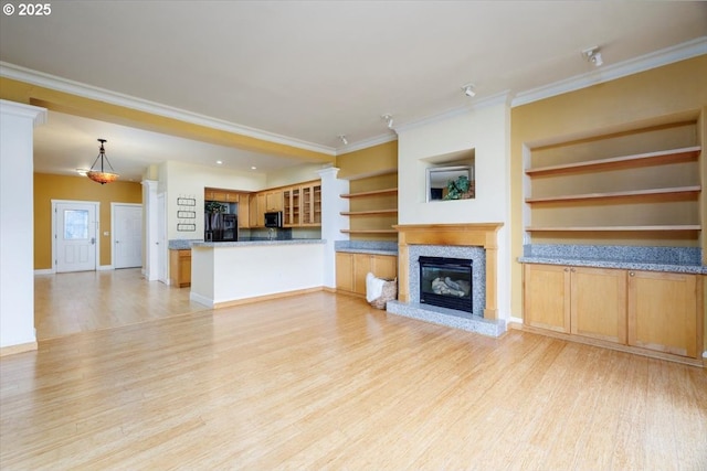 unfurnished living room with built in features, light wood finished floors, ornamental molding, a glass covered fireplace, and baseboards