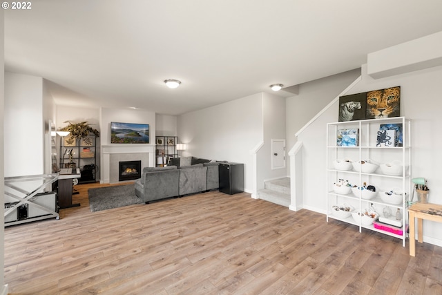 living room featuring light wood finished floors, a glass covered fireplace, and stairs