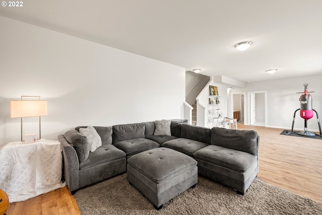 living area featuring baseboards, light wood-style flooring, and stairs
