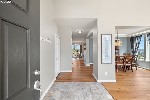 foyer with an inviting chandelier, baseboards, plenty of natural light, and light wood-style flooring