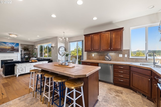 kitchen featuring a notable chandelier, a sink, tile counters, a kitchen bar, and stainless steel dishwasher