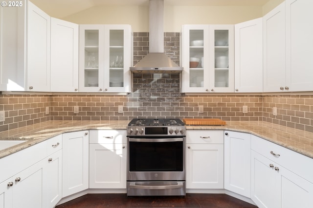 kitchen with white cabinetry, decorative backsplash, stainless steel gas stove, light stone counters, and wall chimney exhaust hood