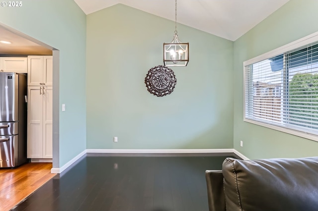 dining space featuring lofted ceiling, a notable chandelier, wood finished floors, and baseboards