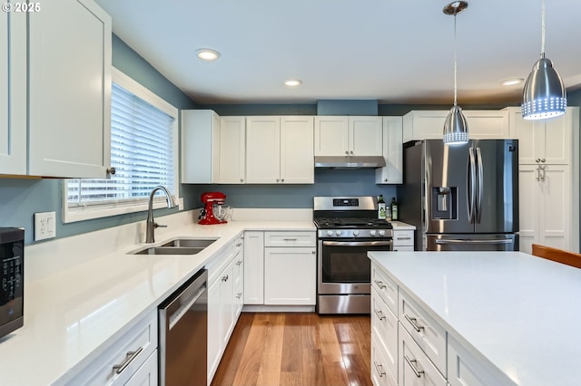 kitchen with wood finished floors, a sink, white cabinets, under cabinet range hood, and appliances with stainless steel finishes