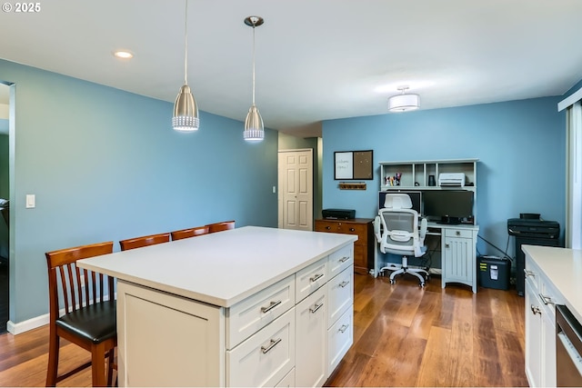 kitchen with dark wood-style floors, a breakfast bar, light countertops, white cabinets, and decorative light fixtures