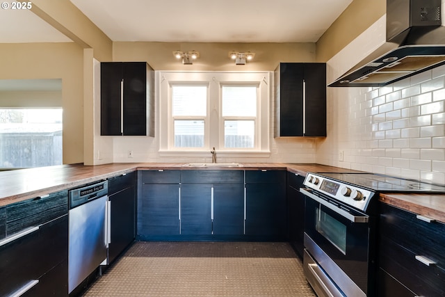 kitchen featuring appliances with stainless steel finishes, wood counters, sink, decorative backsplash, and wall chimney exhaust hood