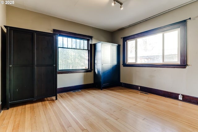 unfurnished bedroom with multiple windows, rail lighting, and light hardwood / wood-style flooring