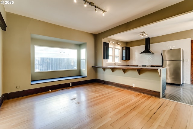 interior space with wall chimney exhaust hood, stainless steel fridge, a kitchen breakfast bar, kitchen peninsula, and light hardwood / wood-style floors