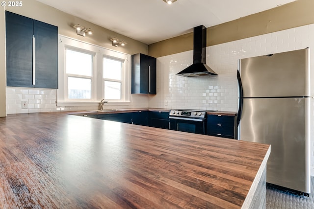 kitchen with appliances with stainless steel finishes, butcher block countertops, sink, kitchen peninsula, and wall chimney exhaust hood