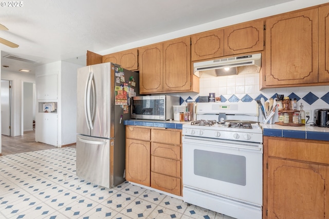1453 N St, Springfield, OR 97477 - kitchen featuring under cabinet range hood, appliances with stainless steel finishes, backsplash, tile countertops, and brown cabinetry