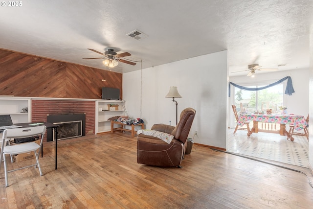 1453 N St, Springfield, OR 97477 - living room featuring ceiling fan, hardwood / wood-style floors, wooden walls, a brick fireplace, and a textured ceiling