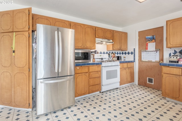 1453 N St, Springfield, OR 97477 - kitchen featuring stainless steel appliances, tile countertops, under cabinet range hood, and backsplash