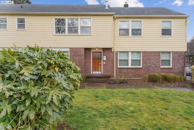 view of front of house with a front yard, a chimney, and brick siding