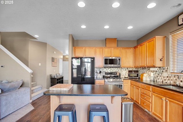 kitchen with a breakfast bar area, stainless steel appliances, dark wood-style flooring, a sink, and dark countertops