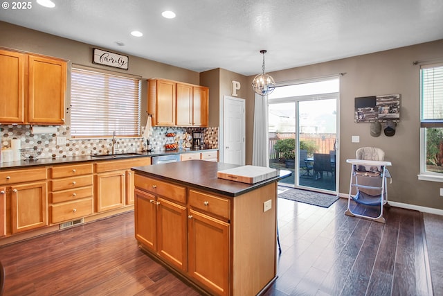 kitchen featuring tasteful backsplash, dark countertops, stainless steel dishwasher, a sink, and plenty of natural light