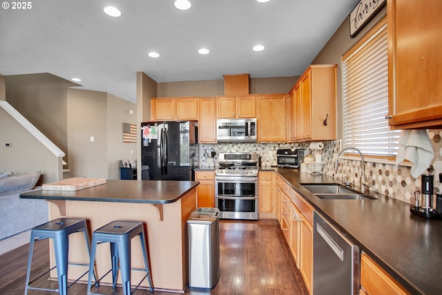 kitchen featuring stainless steel appliances, a sink, a kitchen bar, dark countertops, and dark wood finished floors