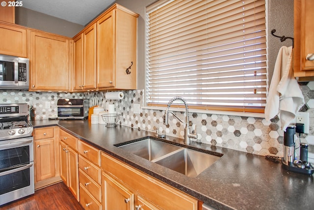 kitchen featuring a toaster, dark wood-style flooring, a sink, appliances with stainless steel finishes, and decorative backsplash