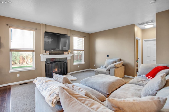 carpeted living area with a glass covered fireplace, visible vents, and baseboards