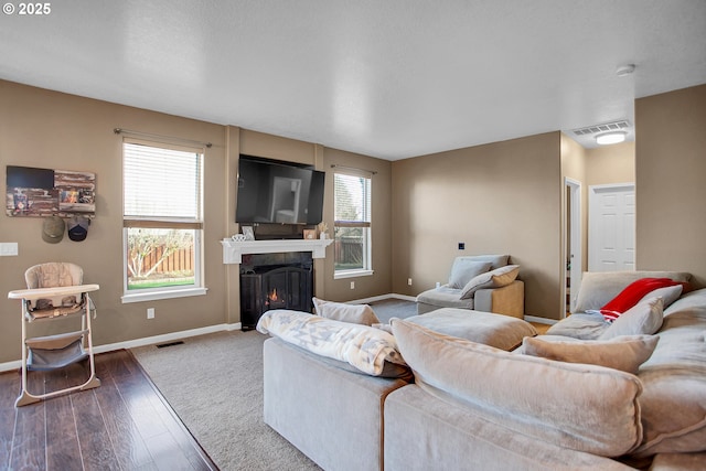 living area featuring visible vents, a lit fireplace, baseboards, and hardwood / wood-style flooring