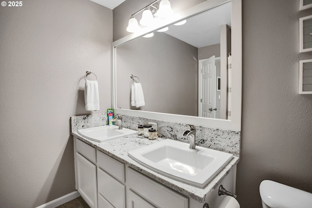 full bathroom with toilet, double vanity, a sink, and a textured wall