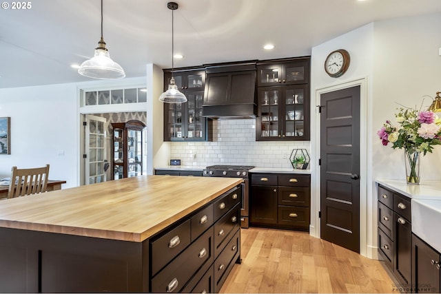 kitchen featuring decorative backsplash, dark brown cabinetry, wooden counters, gas range, and light wood-type flooring