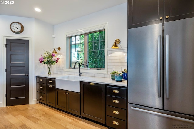 kitchen with a sink, stainless steel refrigerator, decorative backsplash, and light countertops