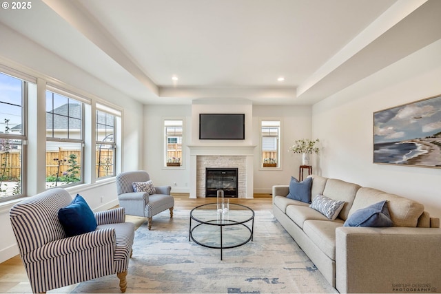 living room with light wood-type flooring, a raised ceiling, a glass covered fireplace, and a healthy amount of sunlight