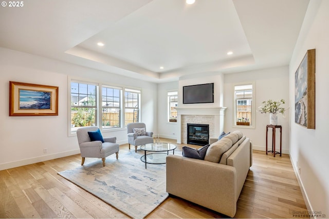 living area with light wood-style floors, a fireplace, a tray ceiling, and recessed lighting