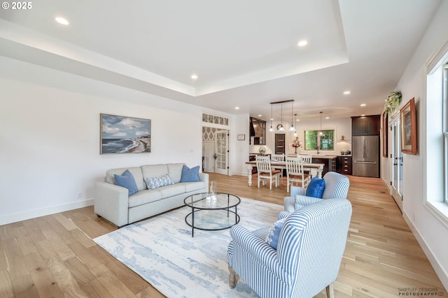 living room with recessed lighting, a tray ceiling, baseboards, and light wood finished floors