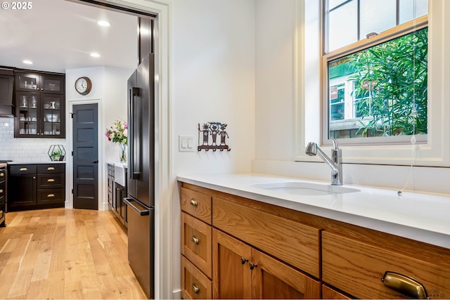 kitchen with glass insert cabinets, light wood-type flooring, recessed lighting, tasteful backsplash, and a sink