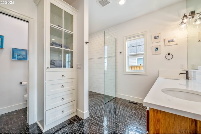 bathroom featuring a walk in shower, a sink, toilet, baseboards, and visible vents