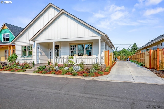 view of front of home featuring board and batten siding, fence, covered porch, and concrete driveway