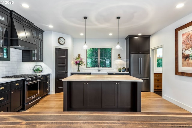 kitchen featuring decorative backsplash, high end appliances, a kitchen island, a sink, and wood counters