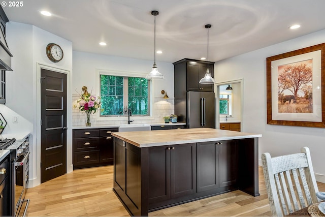 kitchen featuring light wood-type flooring, a sink, wood counters, backsplash, and premium appliances