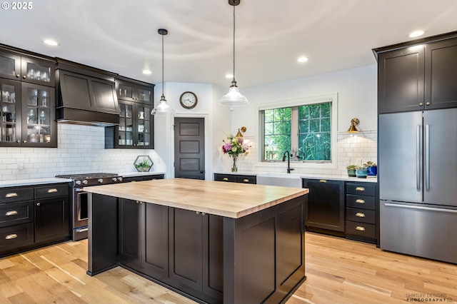 kitchen with appliances with stainless steel finishes, a sink, custom range hood, backsplash, and butcher block counters