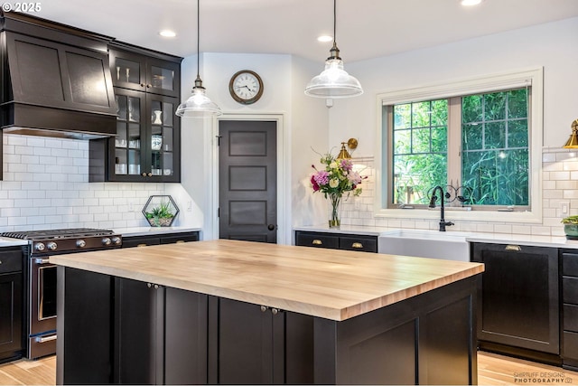kitchen with stainless steel range with gas stovetop, a sink, wood counters, and decorative backsplash