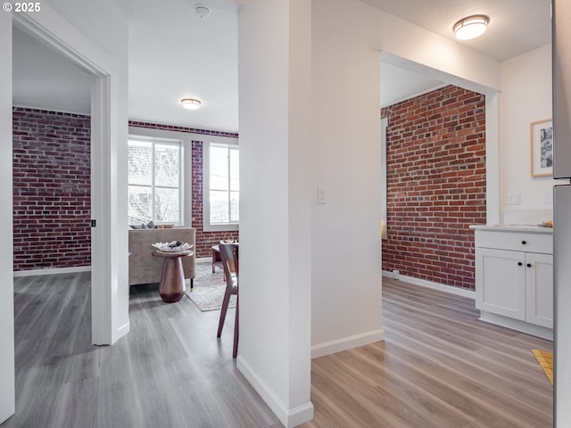 hall featuring brick wall, baseboards, and light wood-type flooring