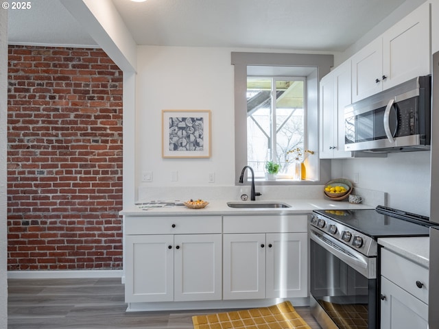 kitchen featuring a sink, light countertops, brick wall, stainless steel appliances, and baseboards