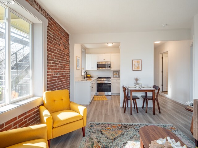 dining room featuring a healthy amount of sunlight, baseboards, light wood-style floors, and brick wall