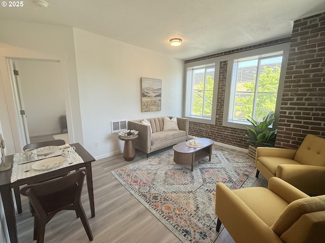 living area featuring visible vents, brick wall, baseboards, a textured ceiling, and light wood-style flooring