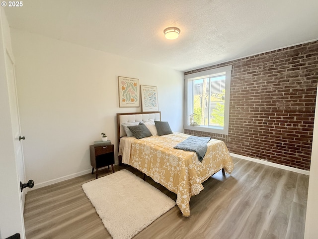 bedroom featuring baseboards, a textured ceiling, brick wall, and light wood-style flooring