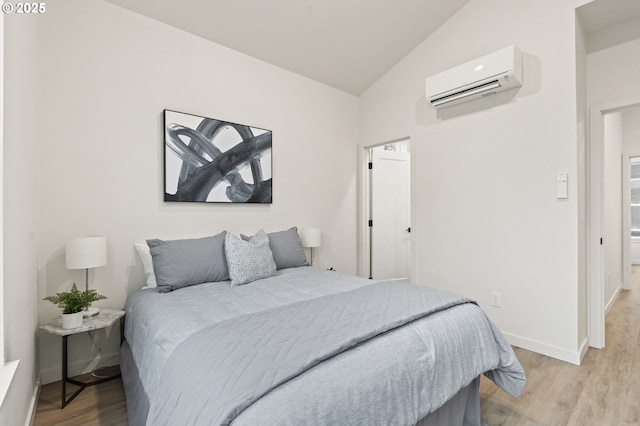 bedroom featuring a wall unit AC, light hardwood / wood-style floors, and vaulted ceiling