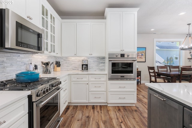 kitchen with appliances with stainless steel finishes, light wood-type flooring, glass insert cabinets, and tasteful backsplash