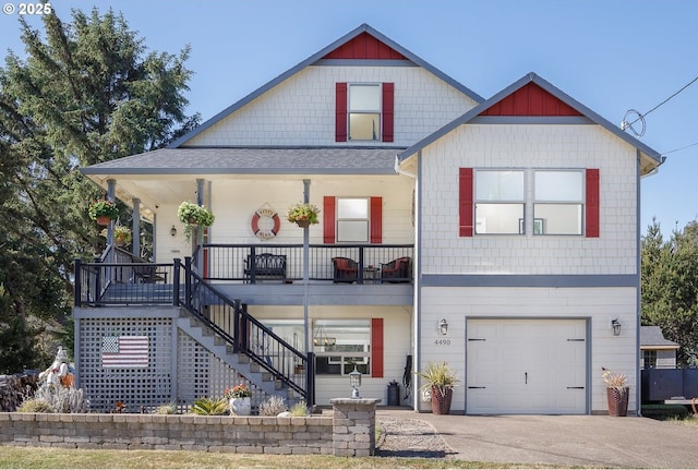 view of front of home featuring roof with shingles, covered porch, stairway, a garage, and driveway