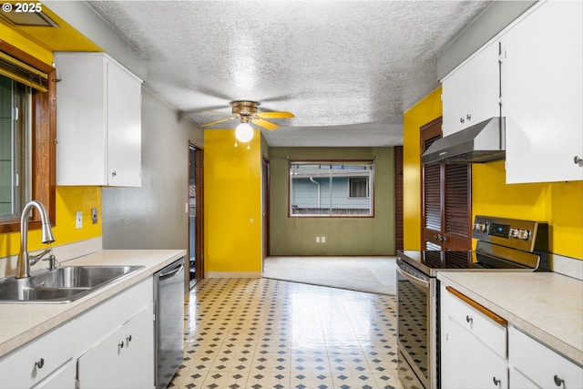 kitchen with appliances with stainless steel finishes, under cabinet range hood, a sink, light countertops, and a textured ceiling